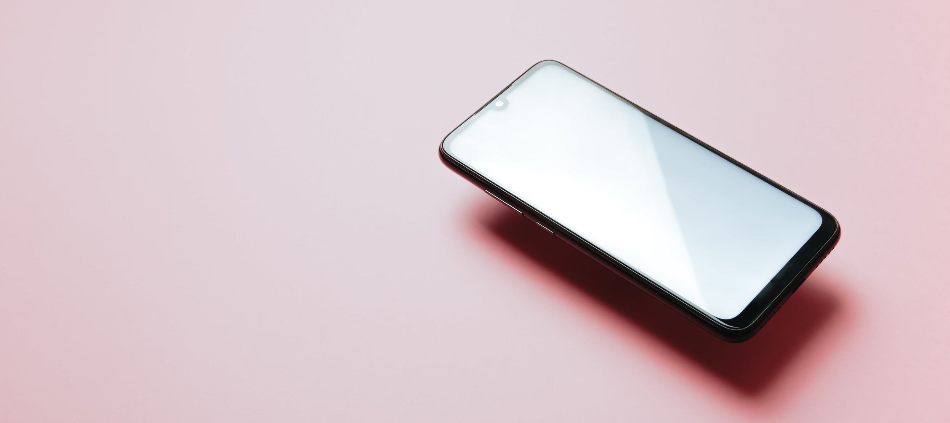 Floating cell phone against a pink background
